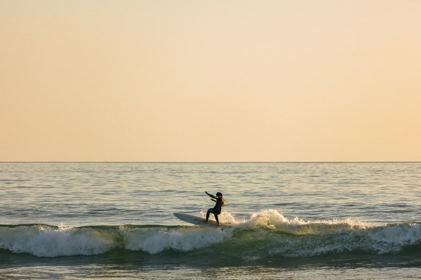 A surfer riding a small wave in warm evening light
